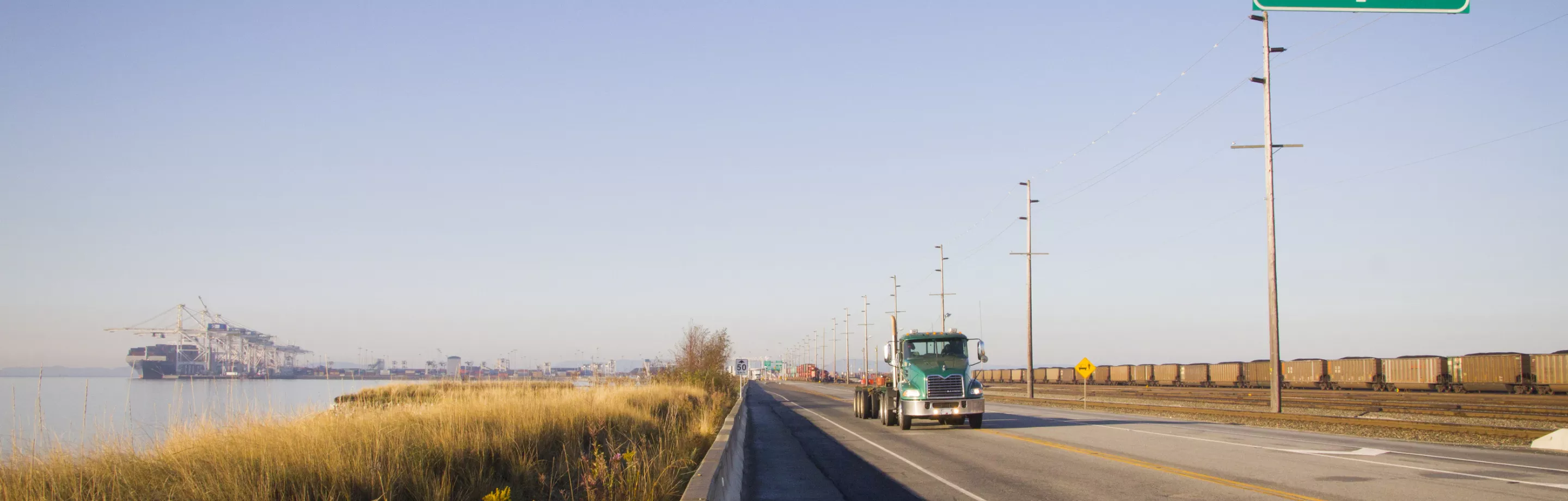 A green container truck drives down a road toward the camera.