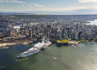 Aerial view of Vancouver, B.C., Canada, showing the downtown area with numerous skyscrapers near the waterfront. Two large cruise ships are docked at Canada Place, a white sail-shaped convention center. 